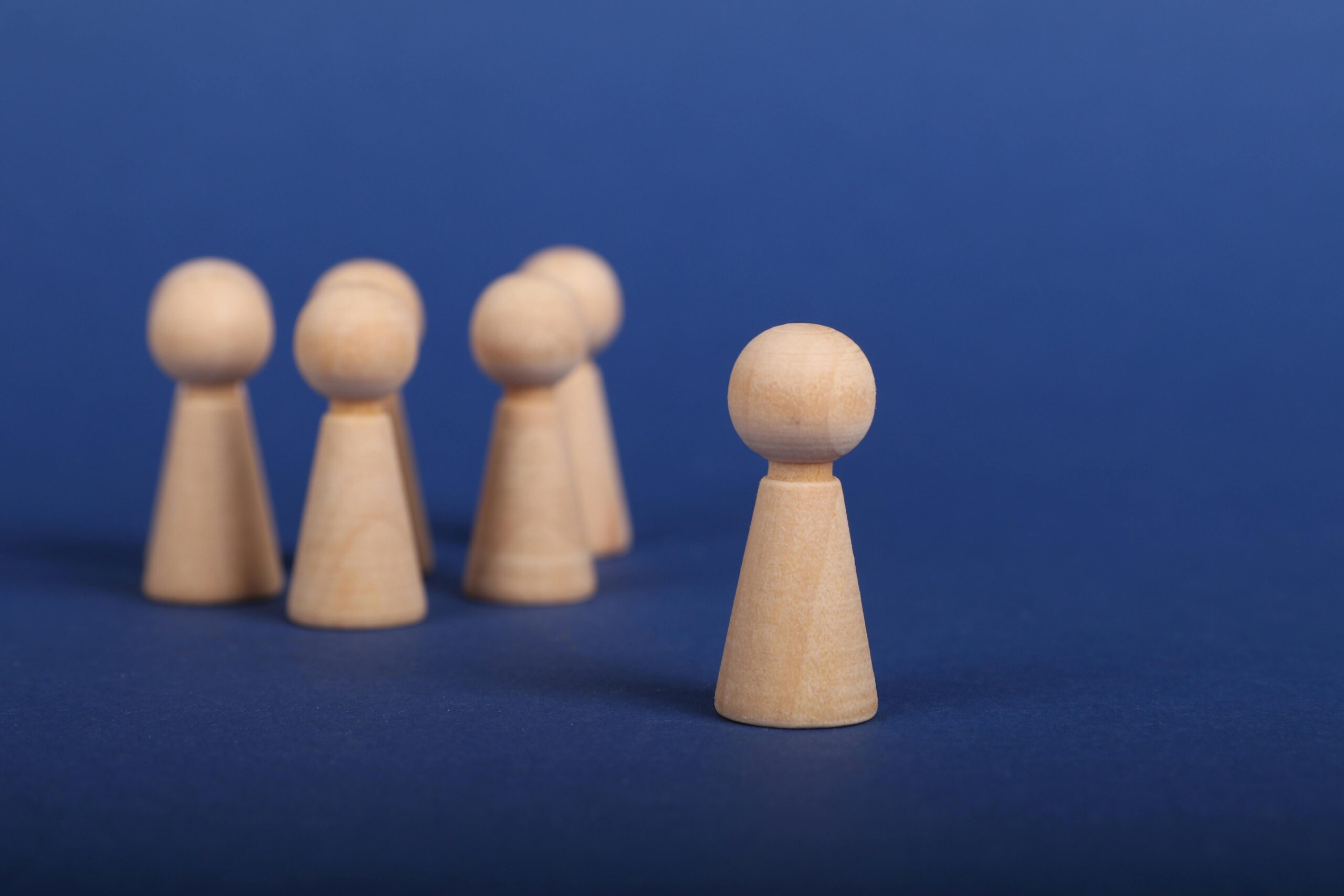 Wooden figures on a blue background depicting a leadership concept with one figure leading a group.
